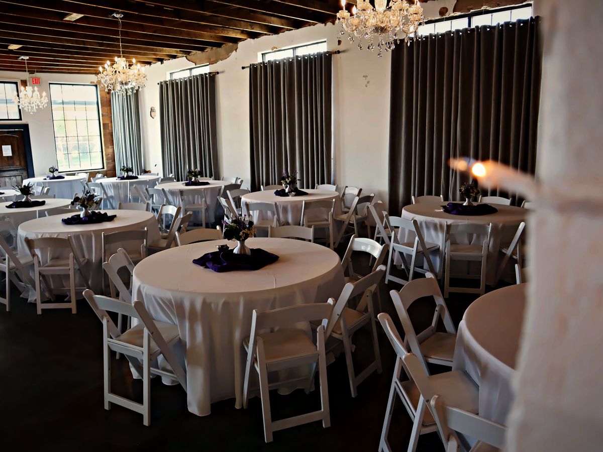 A reception hall set with round tables and white chairs